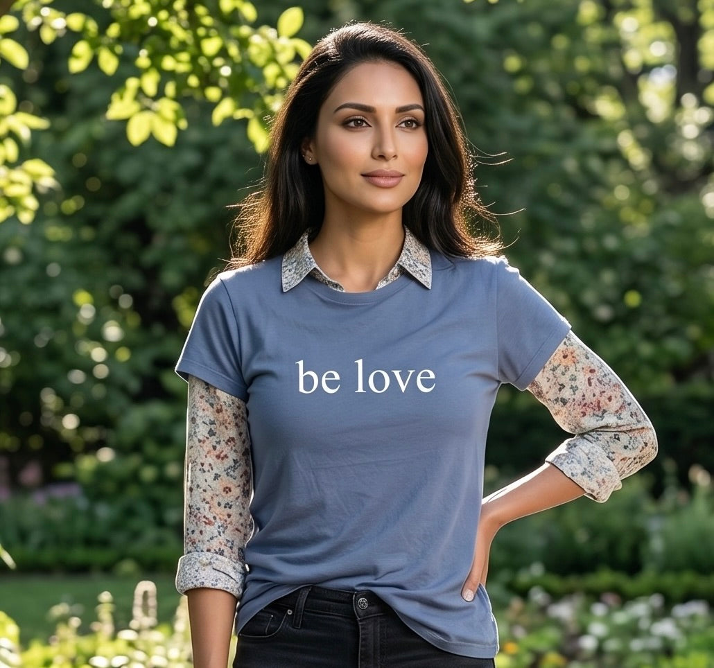 Woman wearing a blue shirt with 'be love' text in a garden setting