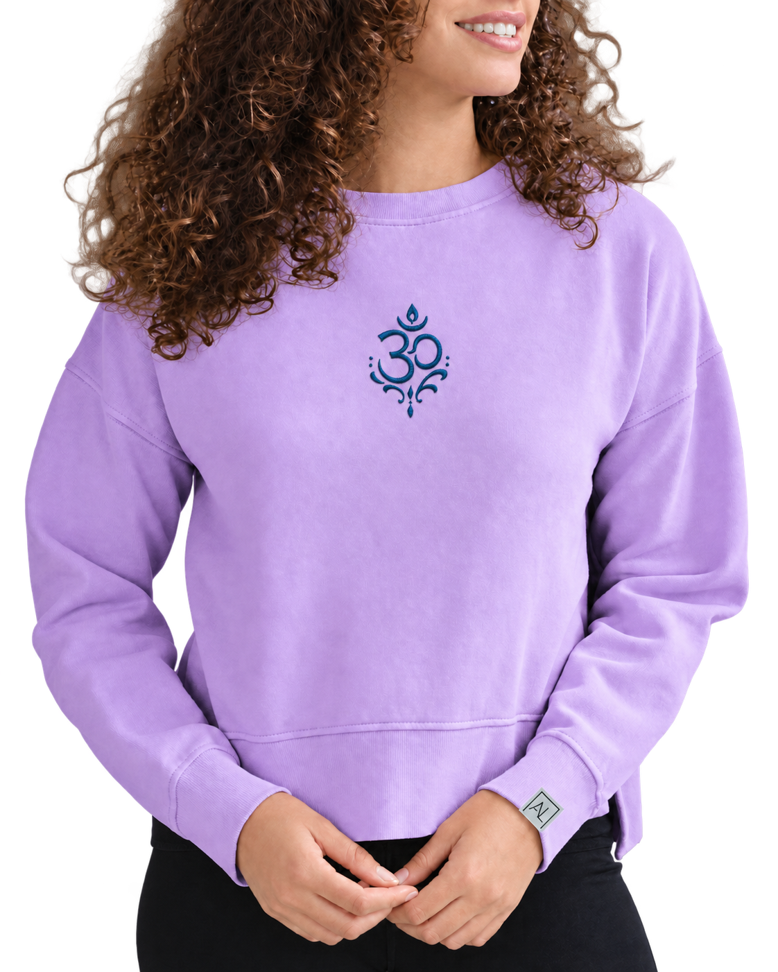 A woman wearing a lavender crewneck sweatshirt with a blue Om symbol printed on the center chest, paired with black pants, against a plain white background.