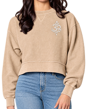 A woman wearing a cropped beige sweatshirt with a white Om symbol on the left chest, paired with blue jeans, shown against a plain white background.